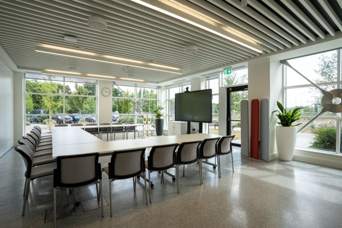 empty meeting room setup with tables, chairs and a monitor in a square formation